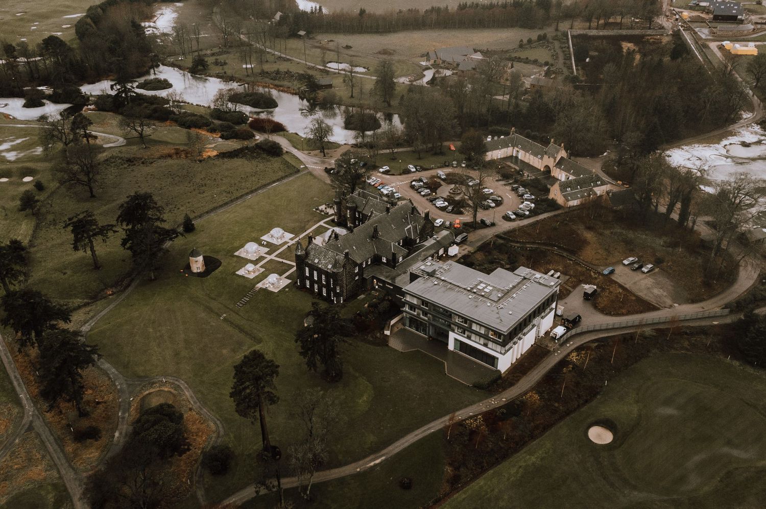 Aerial view of a Scottish estate with multiple buildings nestled among snow-covered grounds and trees.