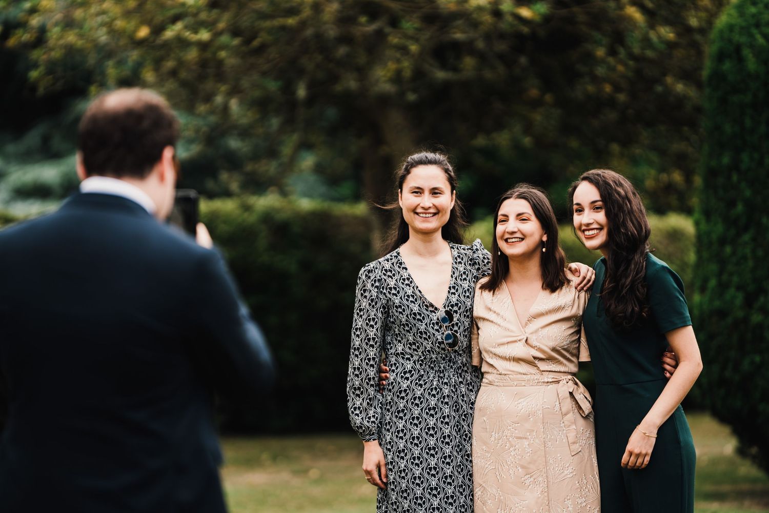 Three friends pose together for a photo outdoors during a wedding celebration.