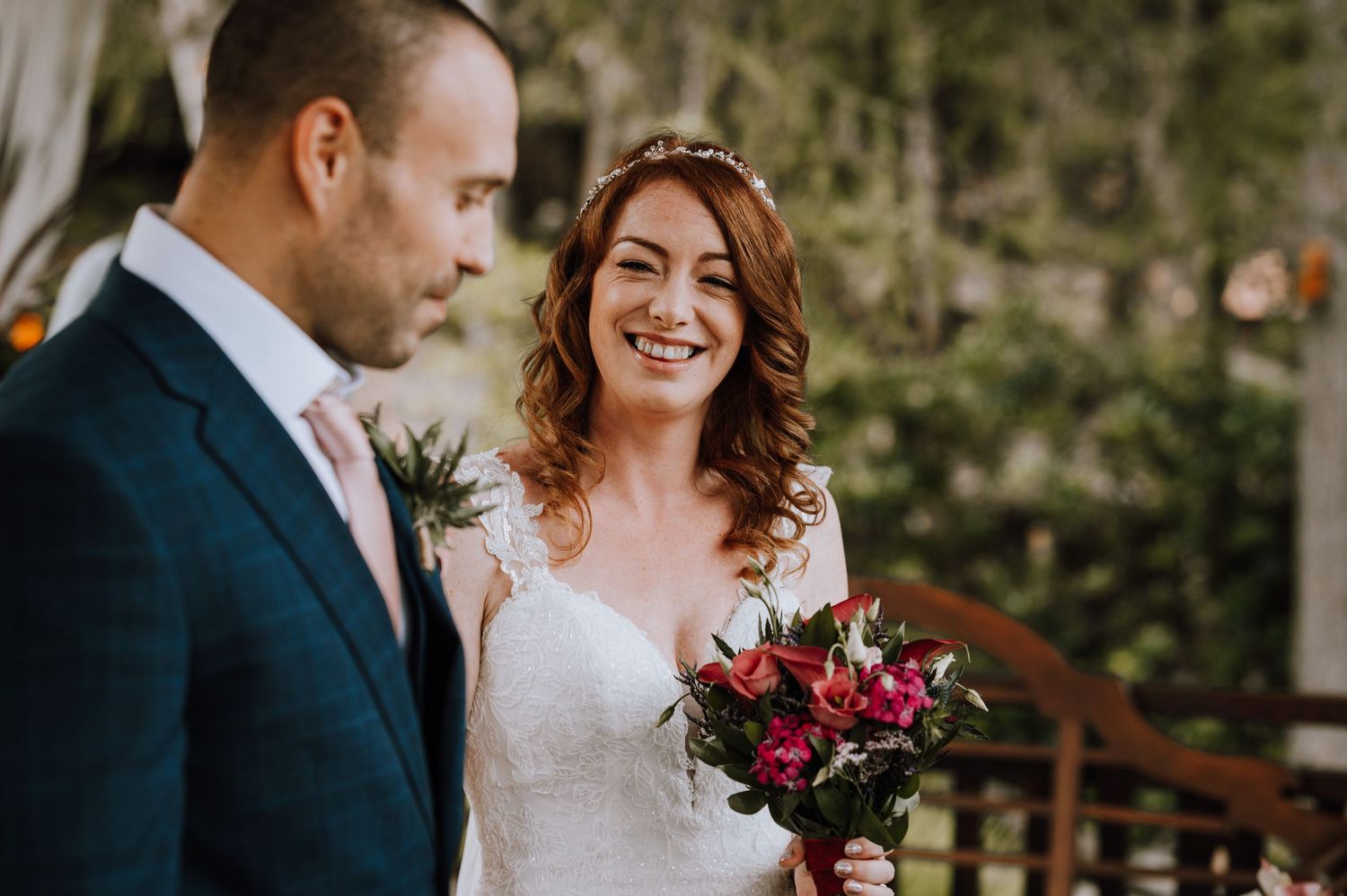 Bride and groom smile at each other during outdoor wedding ceremony.