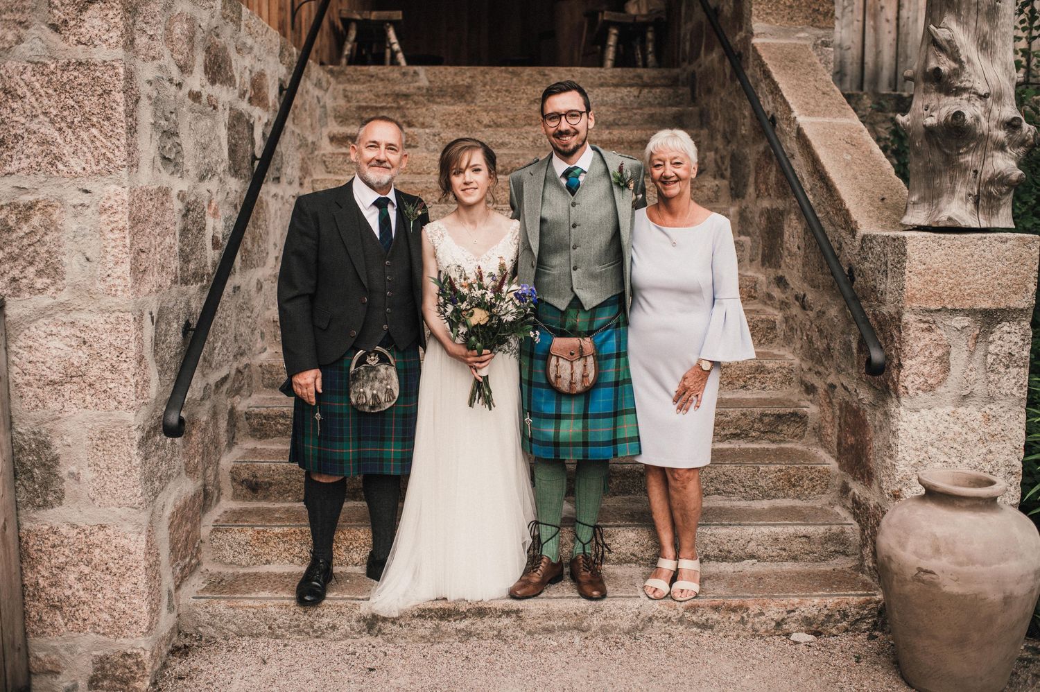 Traditional Scottish wedding party poses on stone steps with kilts and formal attire.