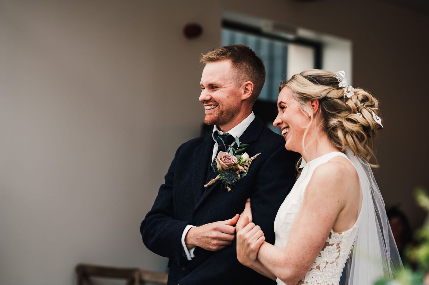 Happy couple laughing together during wedding ceremony under elegant chandeliers.