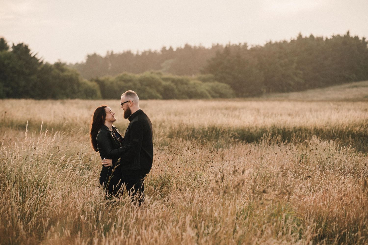 A tender moment between two people standing in a rustic field during sunset.