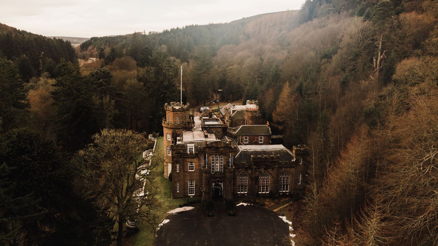 Historic stone mansion nestled in wooded hillside captured from above.