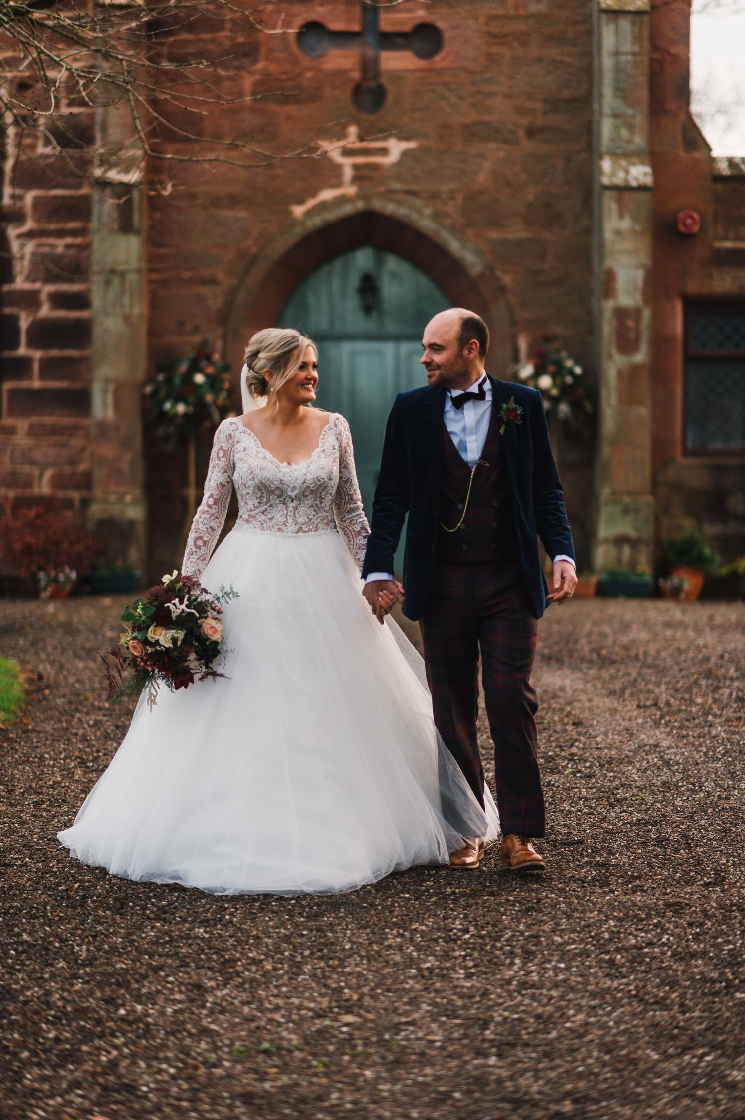 Elegant winter wedding portrait with couple walking along church pathway.