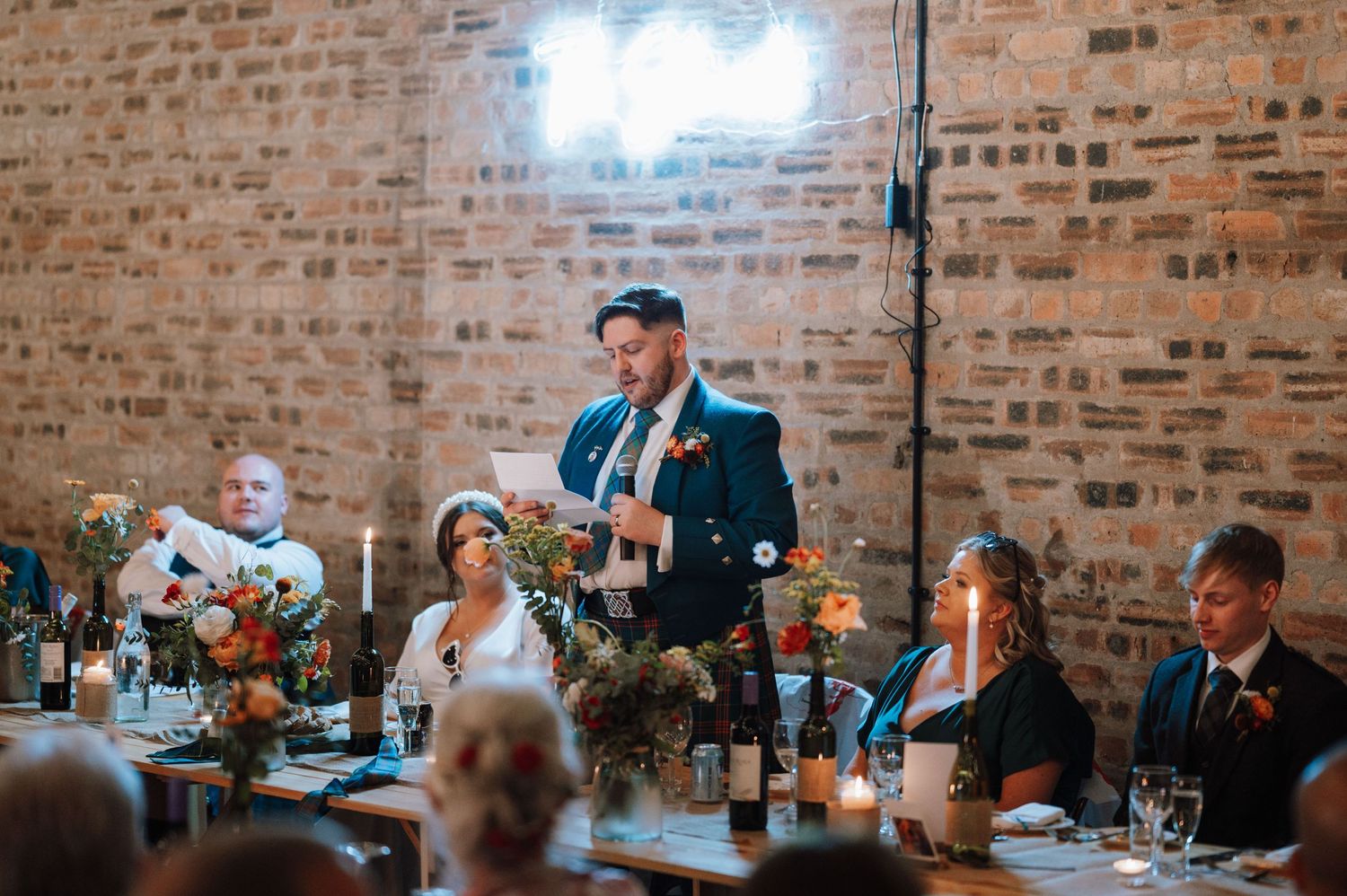 Speech being given during wedding reception dinner in industrial brick venue.