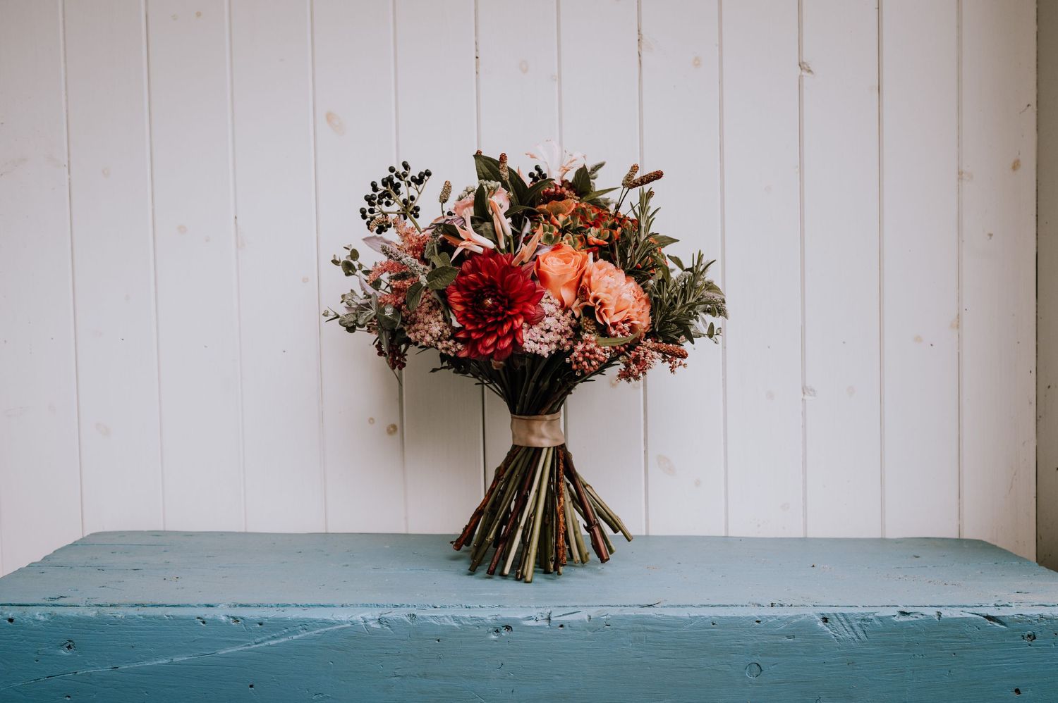 Rustic wedding bouquet with red and pink flowers displayed on blue painted table.