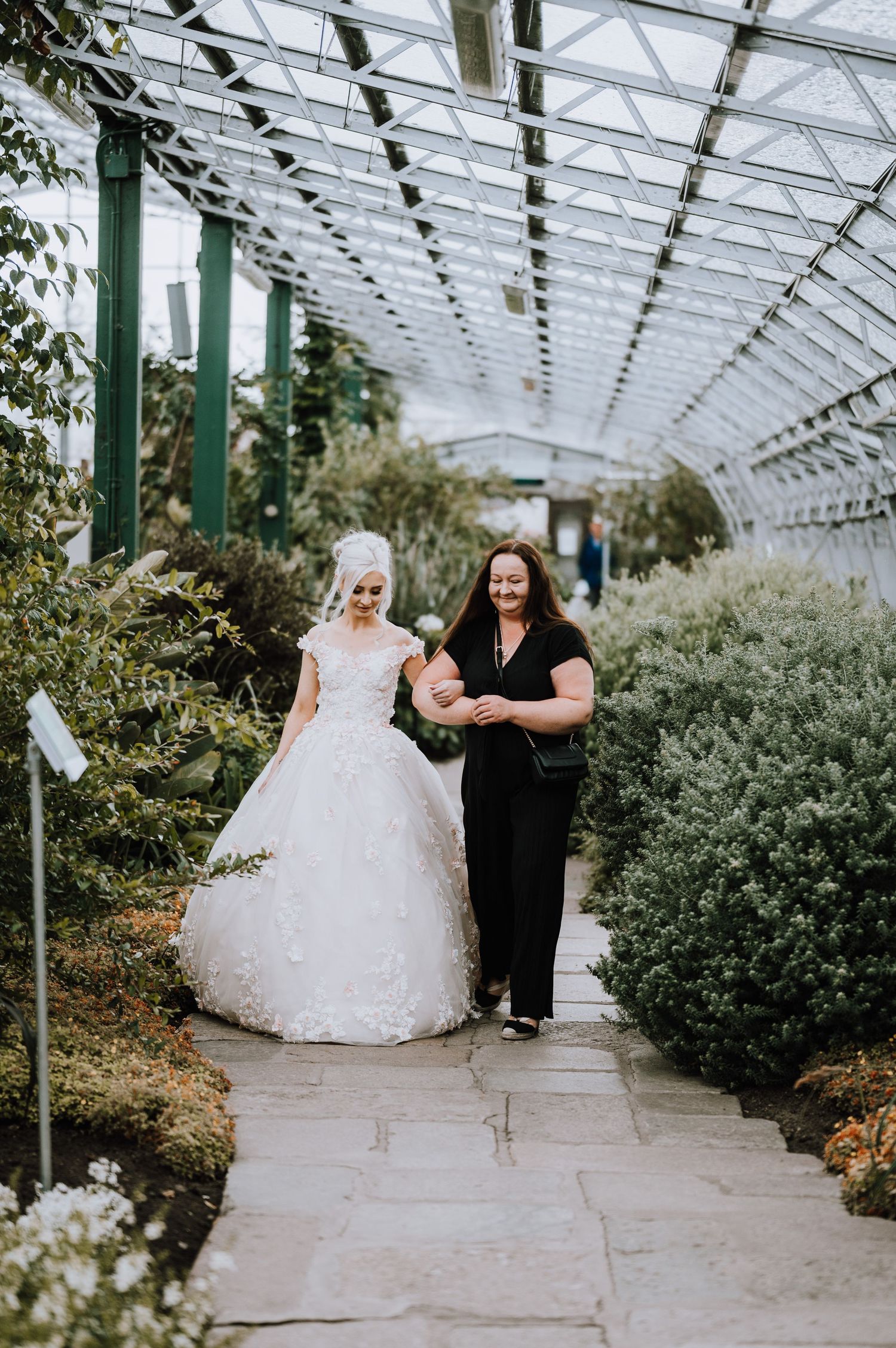 A beautiful wedding dress flowing down a greenhouse pathway lined with plants.