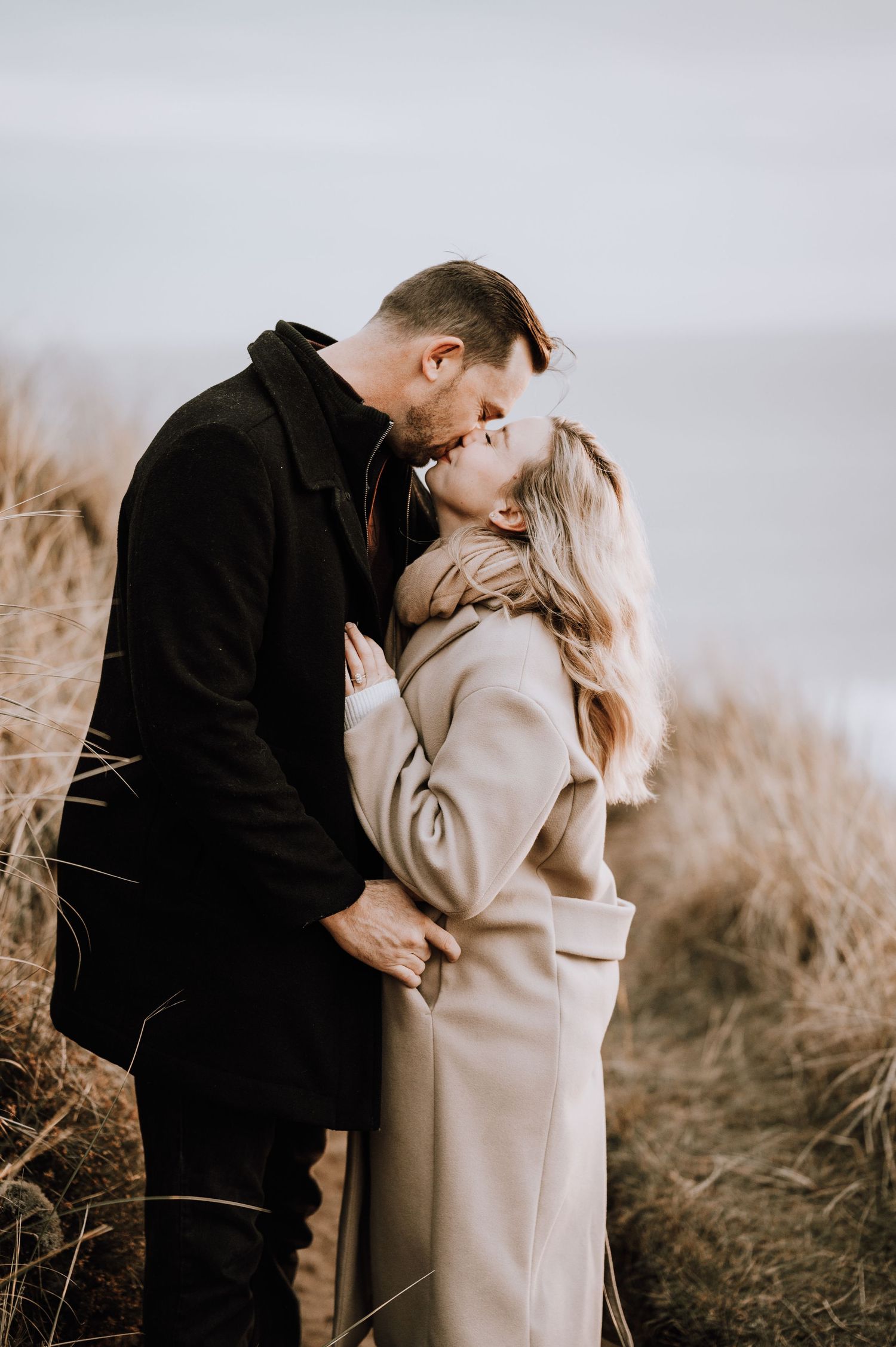 Intimate moment captured between couple on windswept coastal hillside.