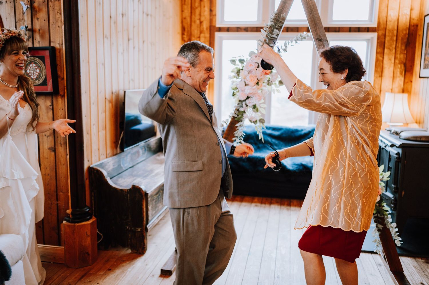 Wedding guests dancing and celebrating in a rustic wood-paneled reception venue.