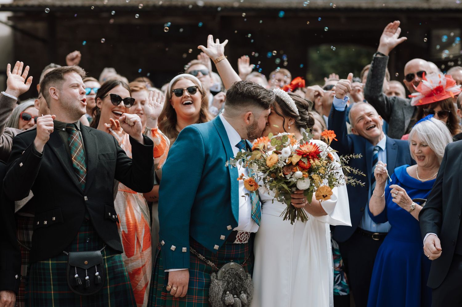 Wedding guests celebrate outdoors with confetti and Scottish kilts.