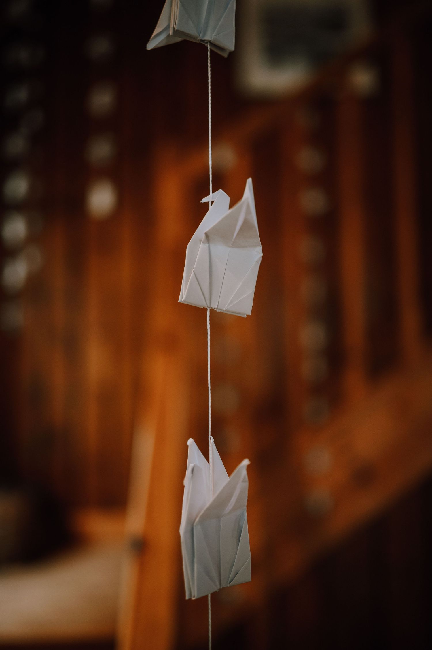 White origami birds hanging on string against wooden wall with warm lighting.