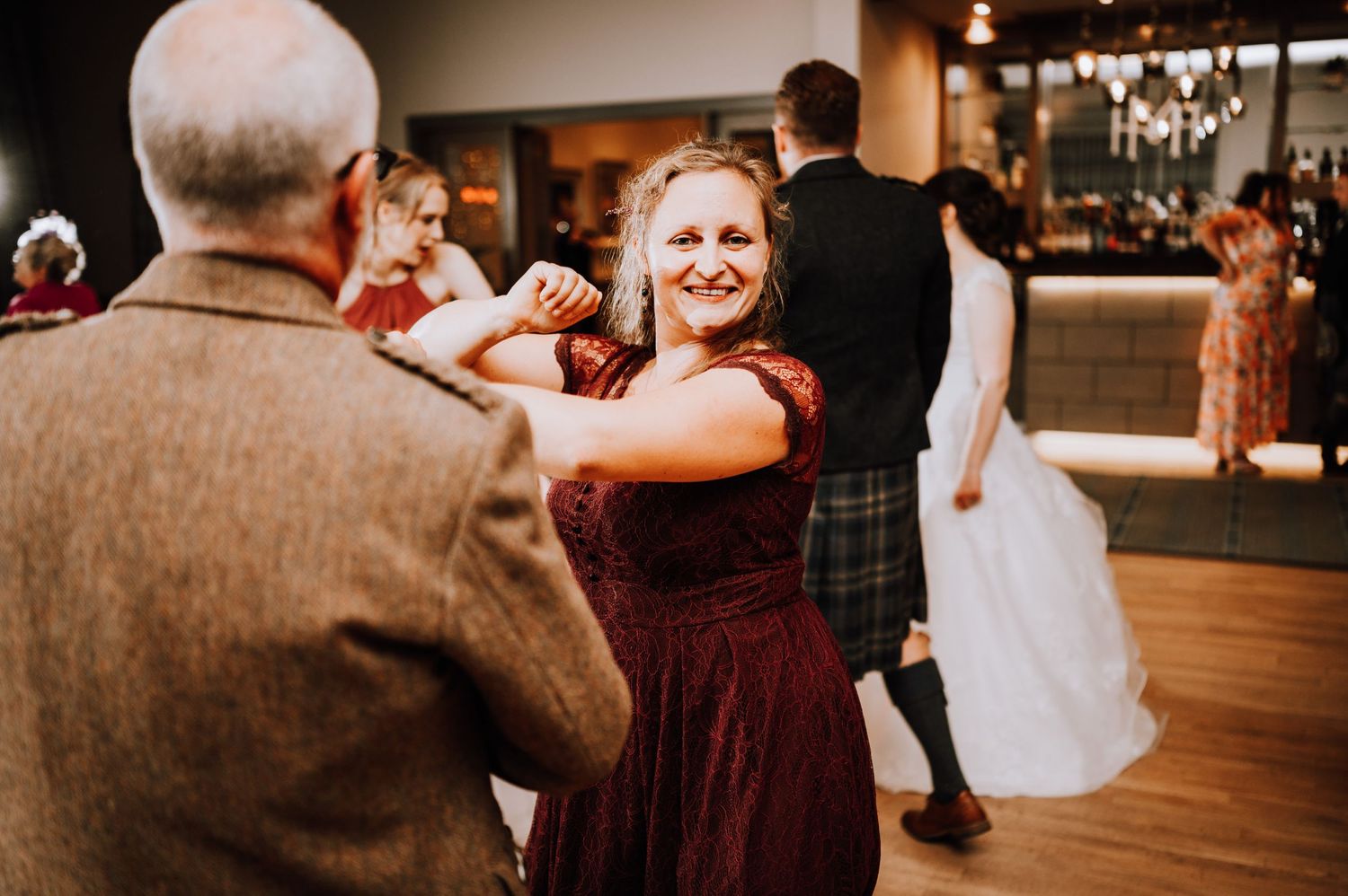 A person in a burgundy dress dances with a partner on a wooden dance floor.