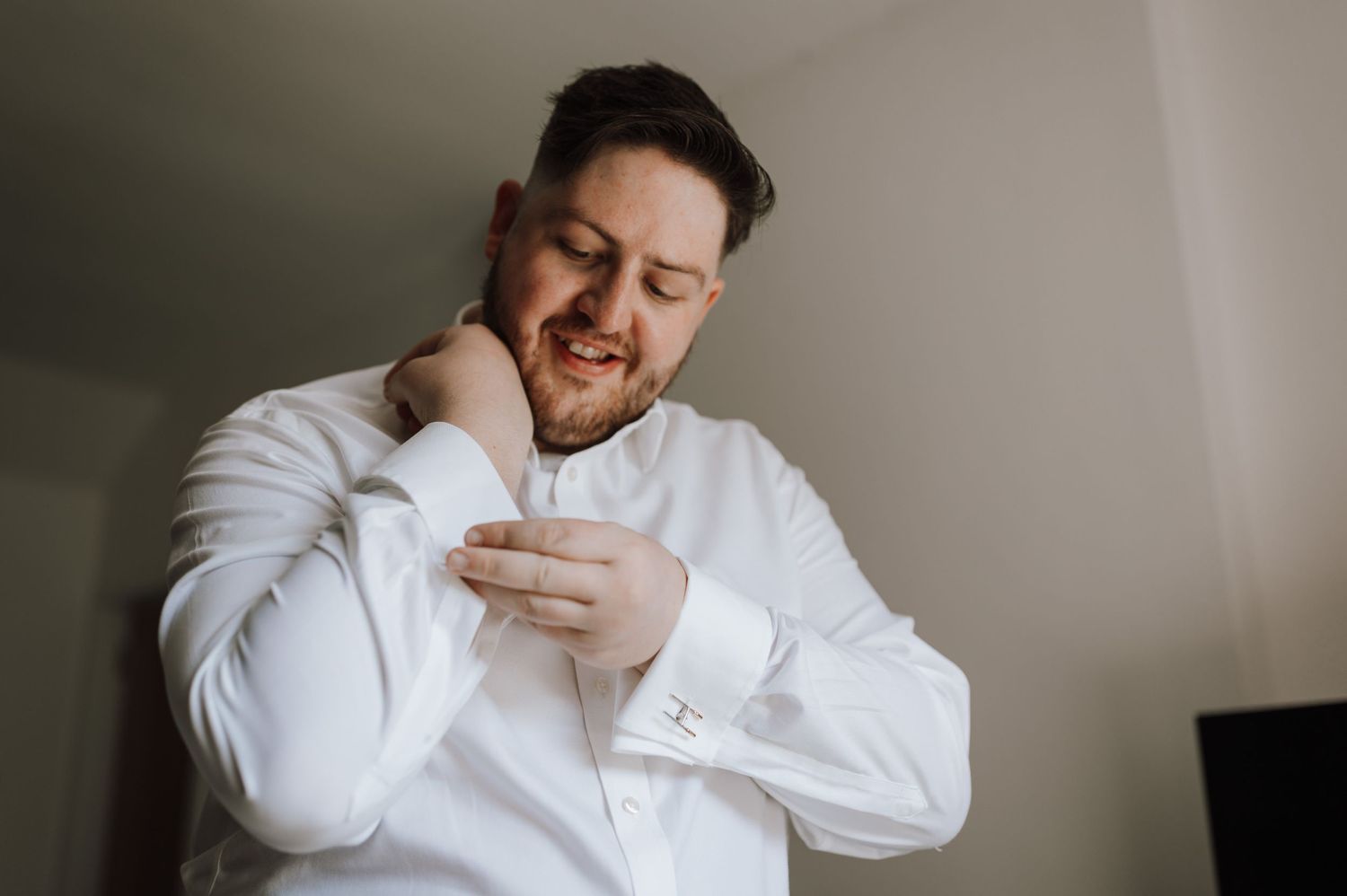 Person in white dress shirt adjusting collar and cuffs.