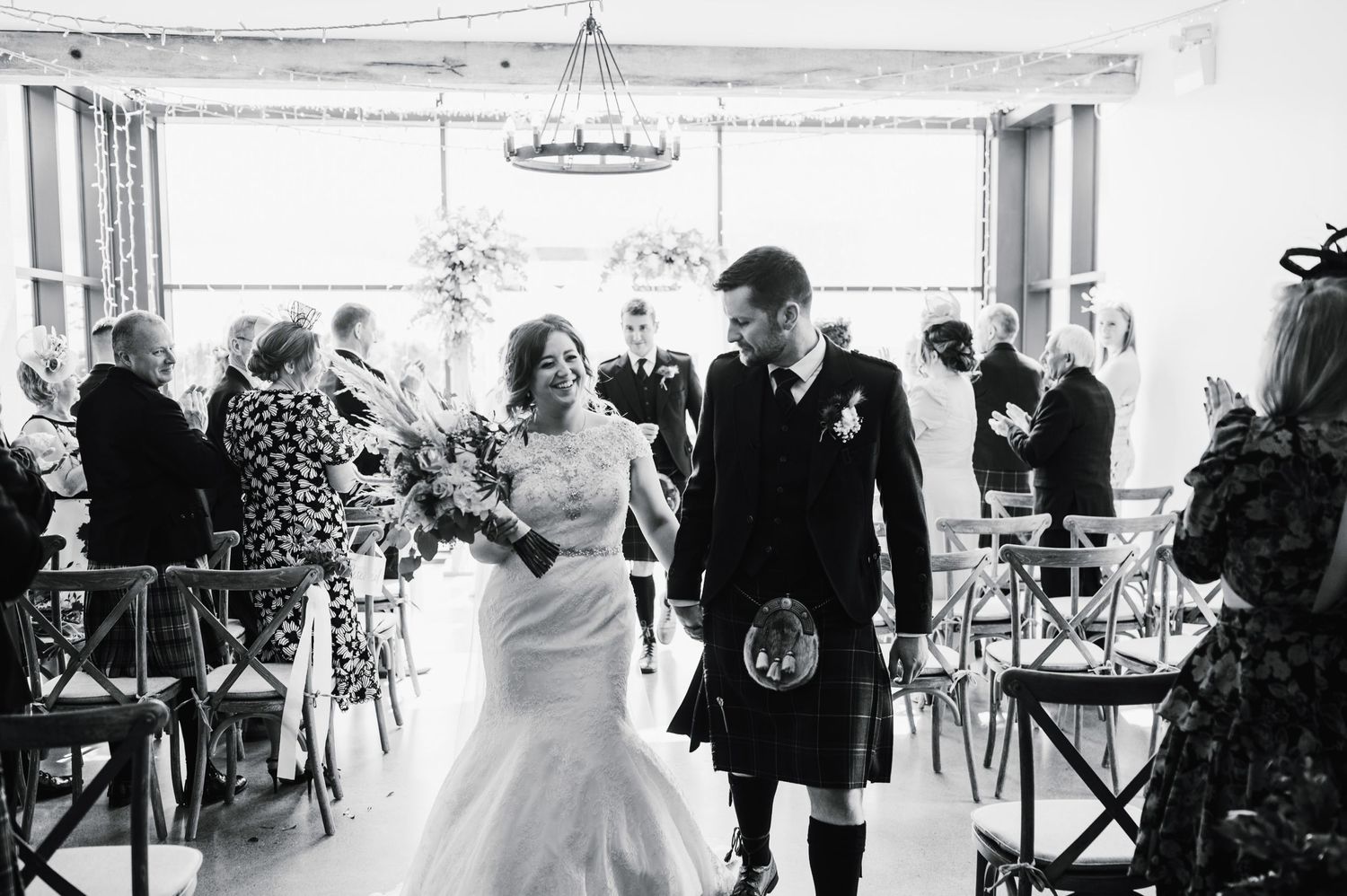 A black and white photo of newlyweds walking down the aisle after their ceremony.