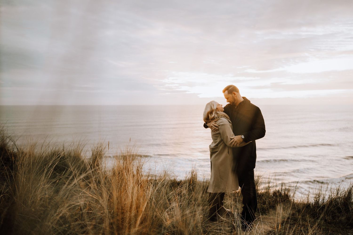Couple standing close together on seaside cliffs during golden hour.