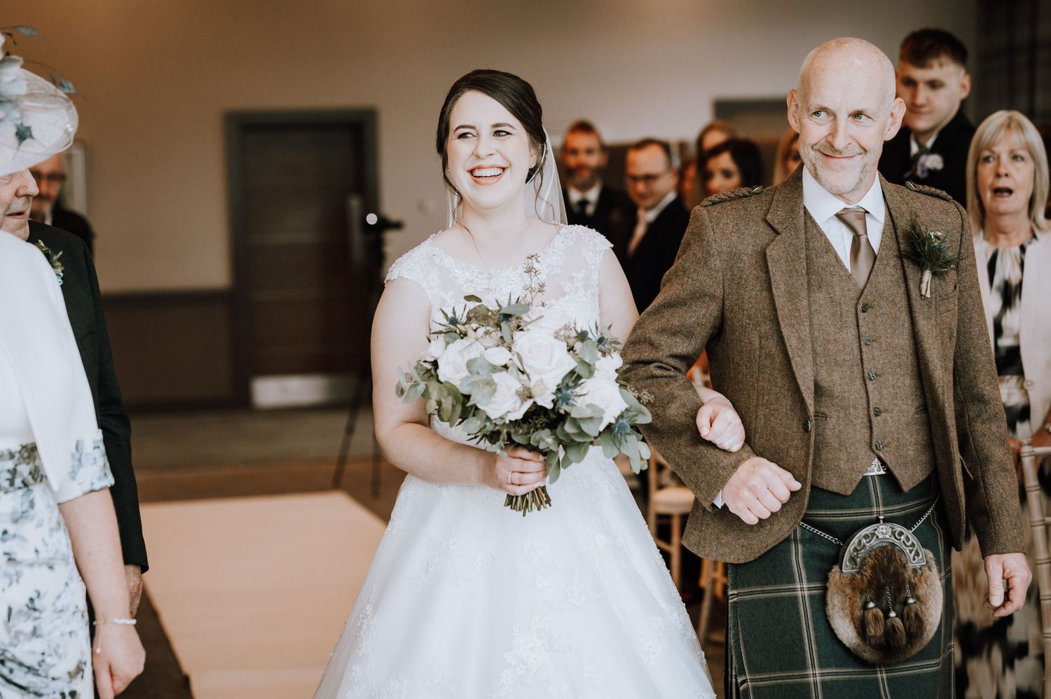 Two men in traditional Scottish kilts share a celebratory moment during a wedding ceremony.
