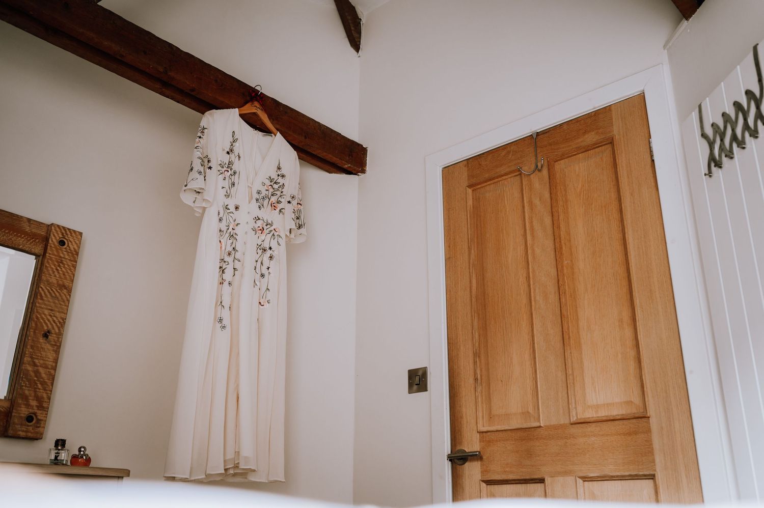 An elegant floral wedding dress hanging in a rustic room with wooden beams and natural light.