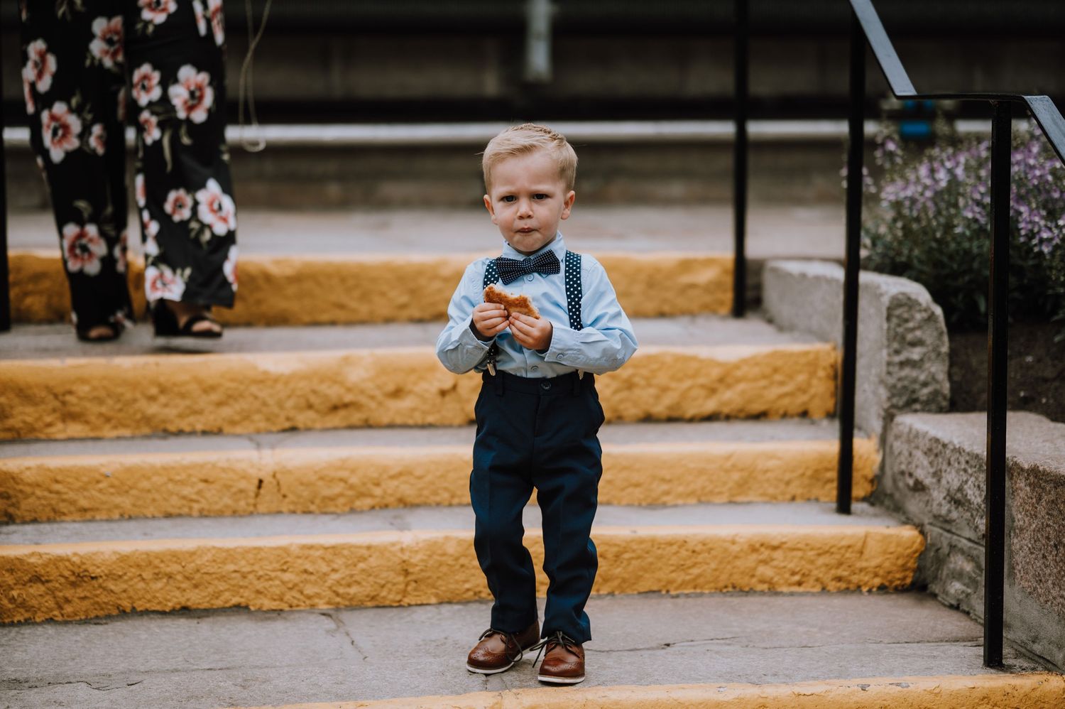A small child in blue overalls and suspenders stands on yellow-painted concrete steps.