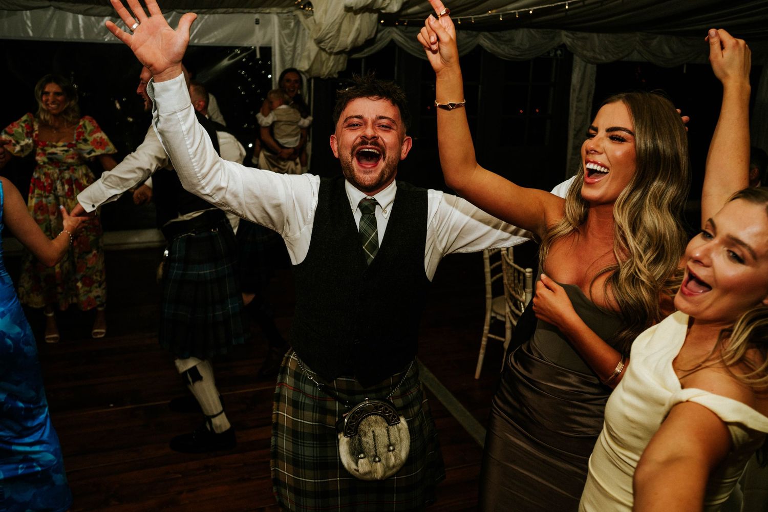 Joyful celebration with hands raised during wedding reception dance party.