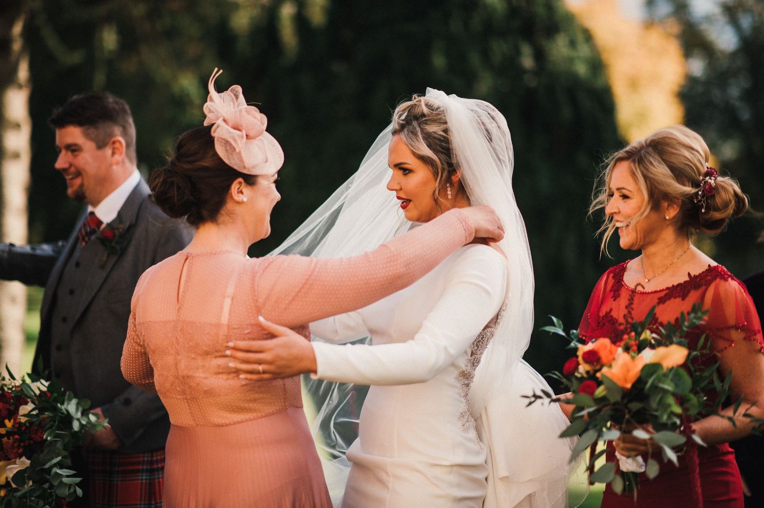 Wedding guests share an emotional moment during an outdoor ceremony with autumn colors in the background.