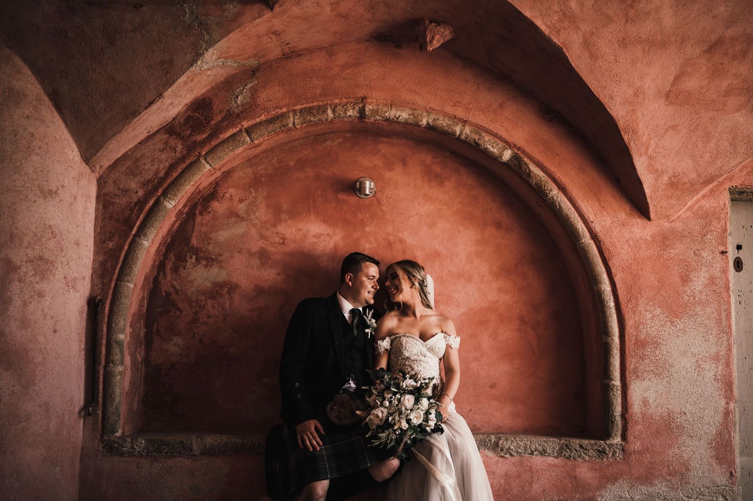 A romantic wedding portrait under a terracotta archway with dramatic lighting.