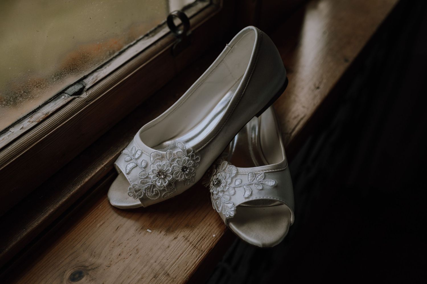 White lace bridal shoes with peep toes sit on wooden surface.