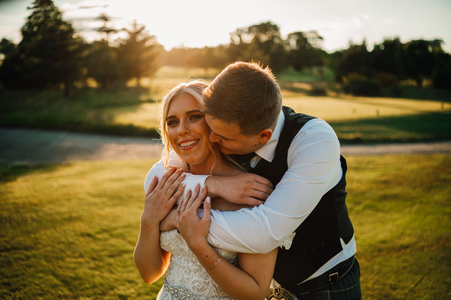 A couple sharing an intimate moment on a golf course at sunset while wearing wedding attire.