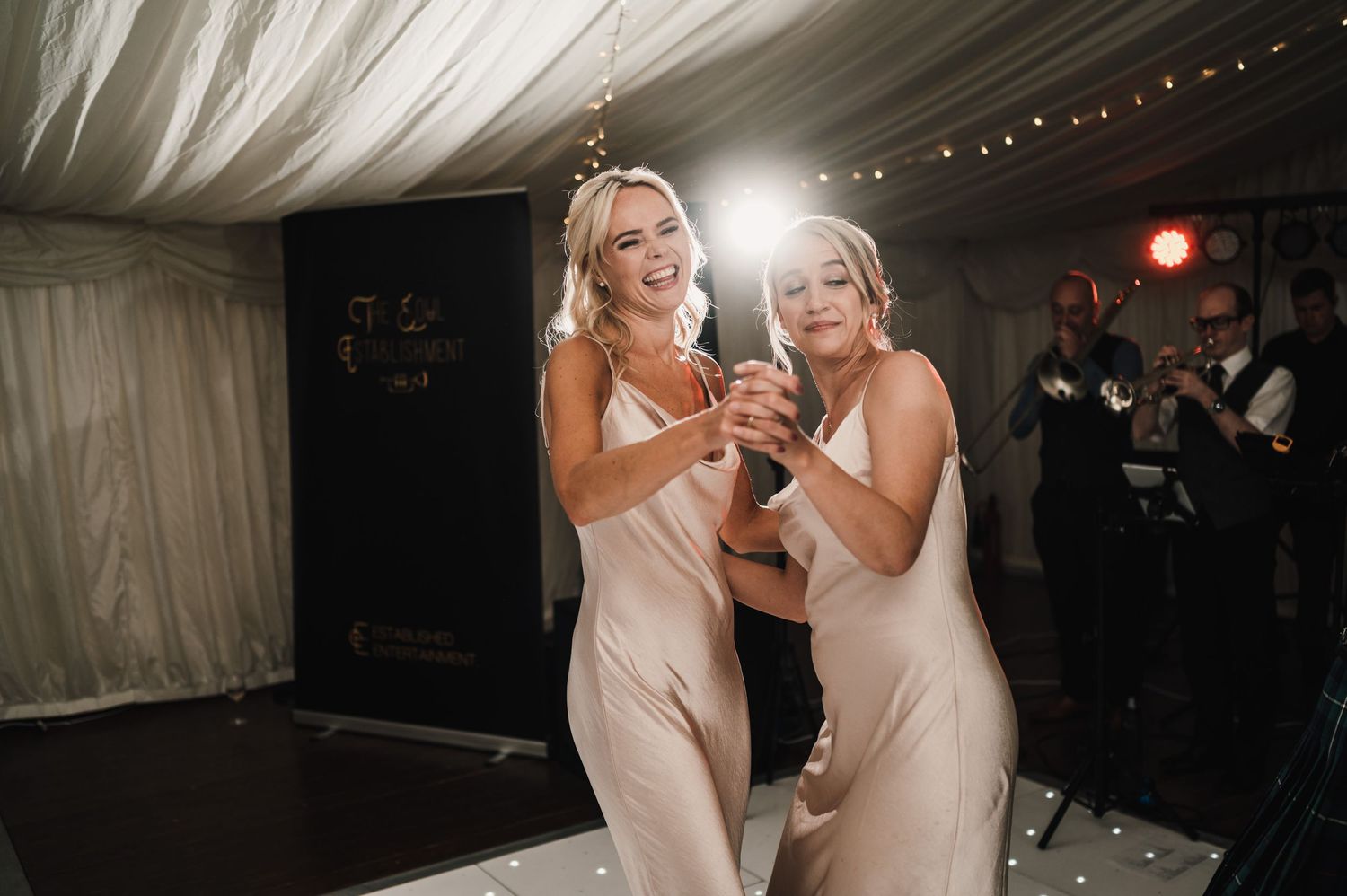 Wedding guests in matching dresses dancing together at an evening reception.