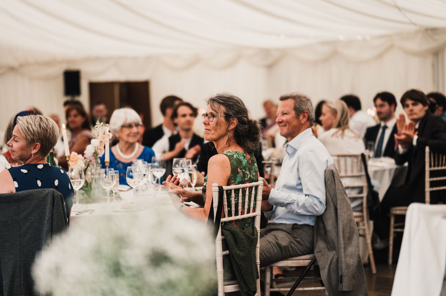 Wedding guests seated at decorated tables under white tent enjoying the reception celebration.