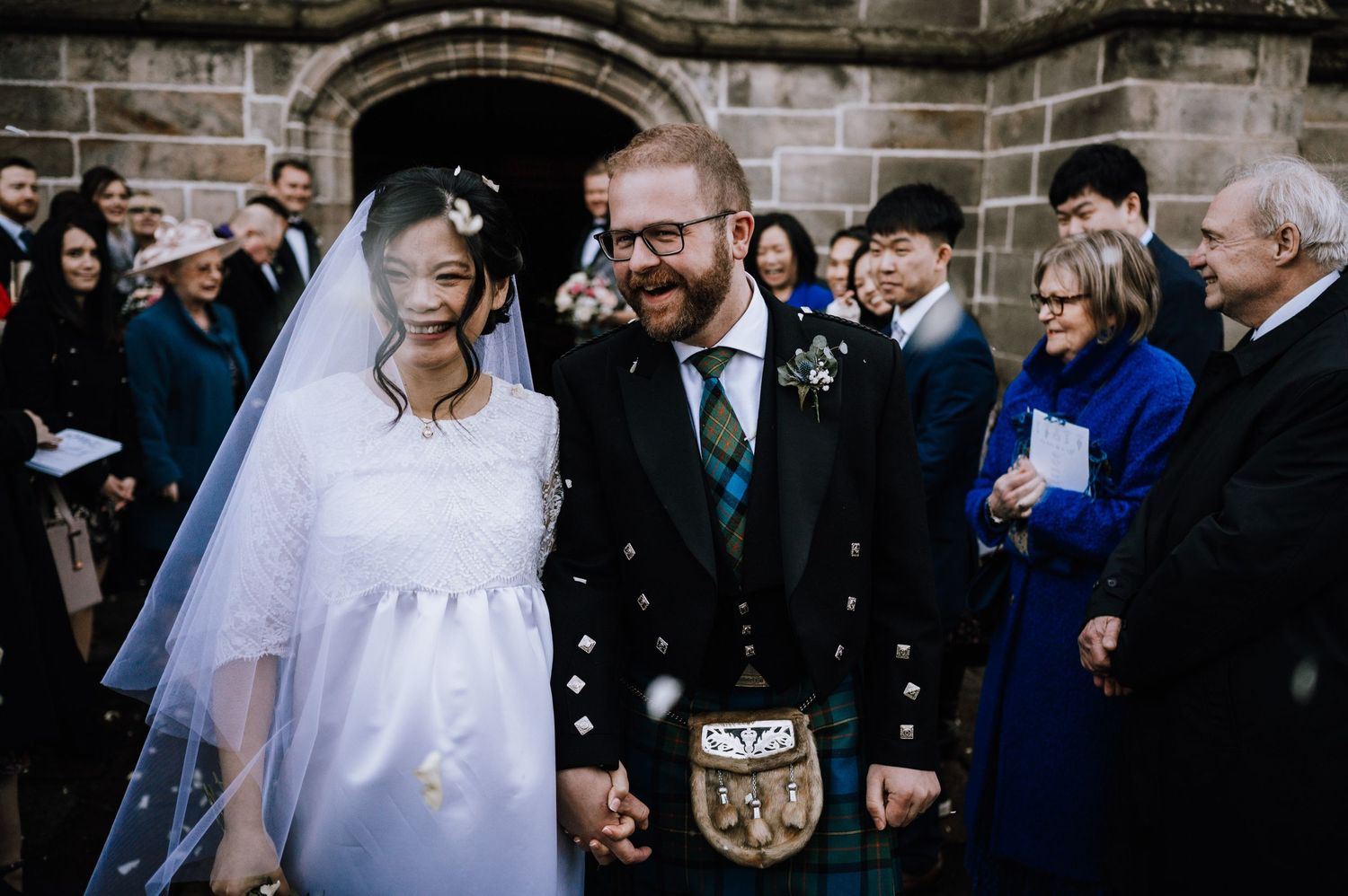Happy couple celebrated with confetti outside historic stone church entrance.