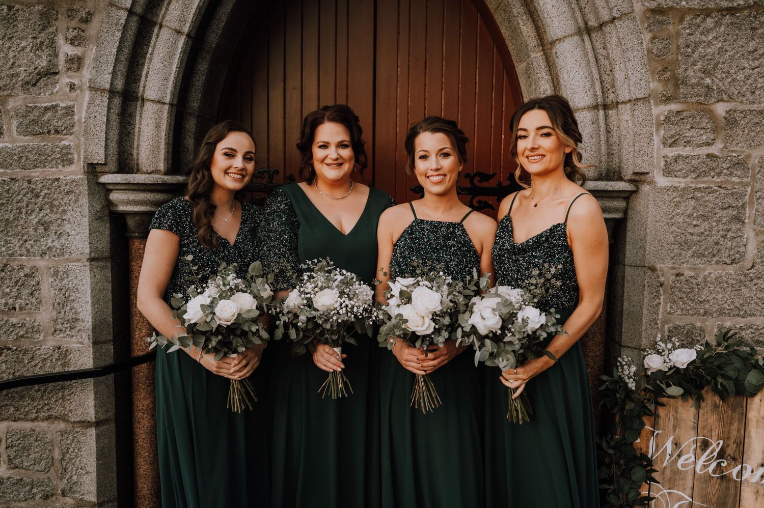 Four bridesmaids in emerald green dresses holding matching floral bouquets.