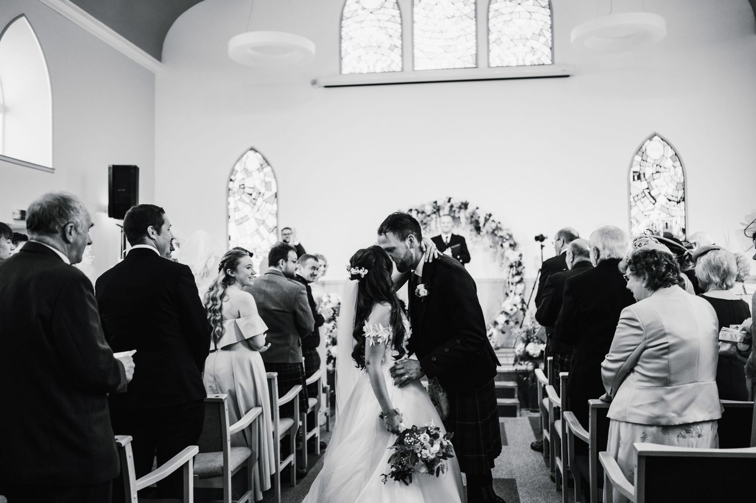 Black and white photograph of a wedding ceremony in a traditional church with arched windows and gathered guests.