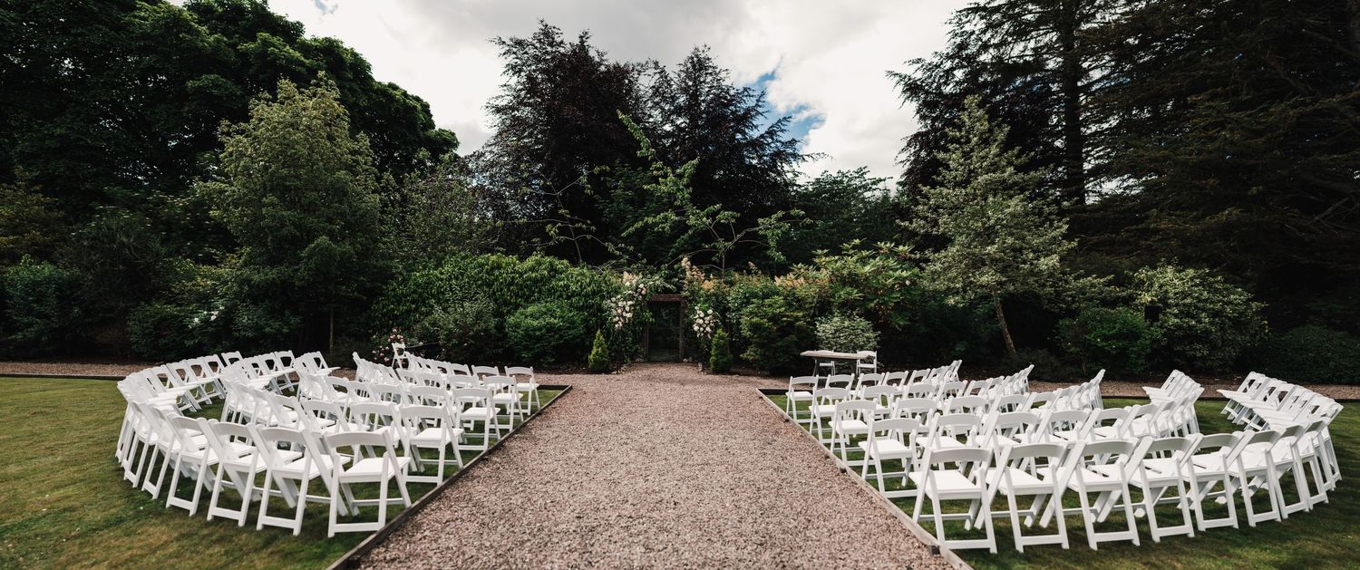 Outdoor wedding ceremony setup with white chairs arranged in curved rows facing a floral arch.