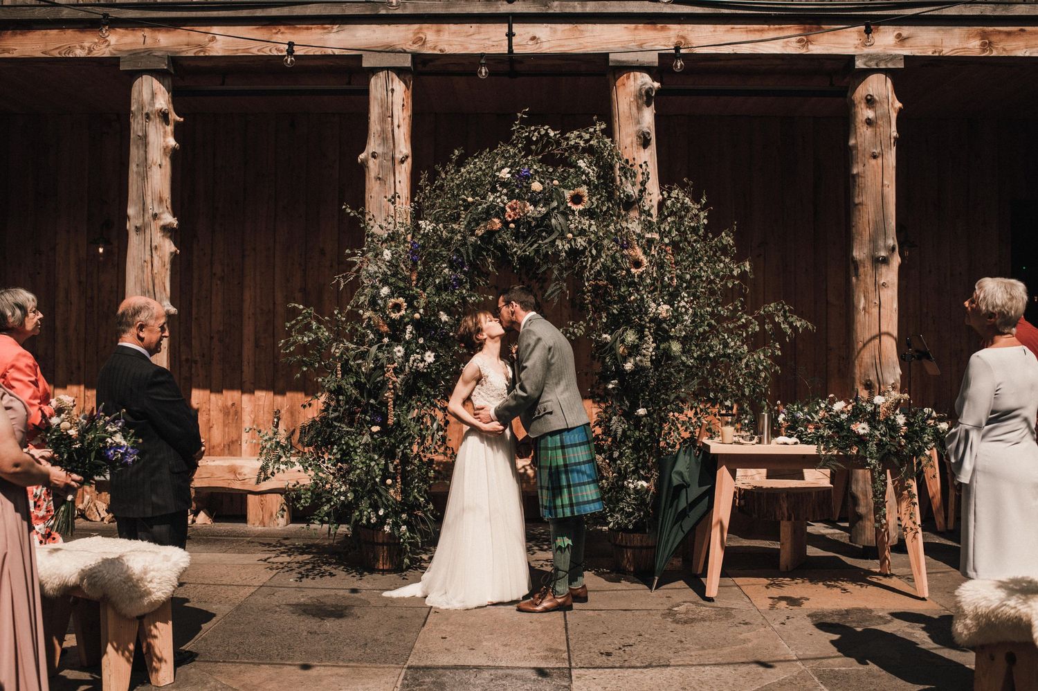 An intimate outdoor wedding ceremony with guests seated on either side of a floral-decorated arch.