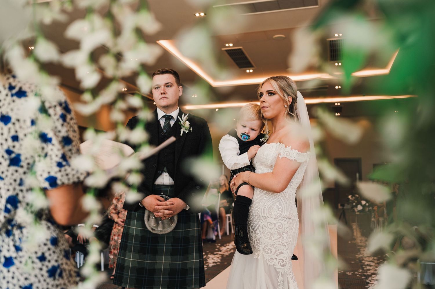 A wedding ceremony with Scottish elements featuring a kilt-wearing groom and bride in lace dress.