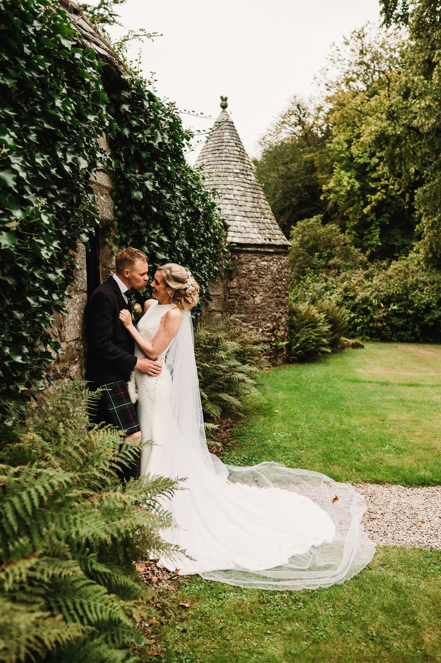 Couple shares intimate moment by ivy-covered stone turret with flowing white wedding veil.