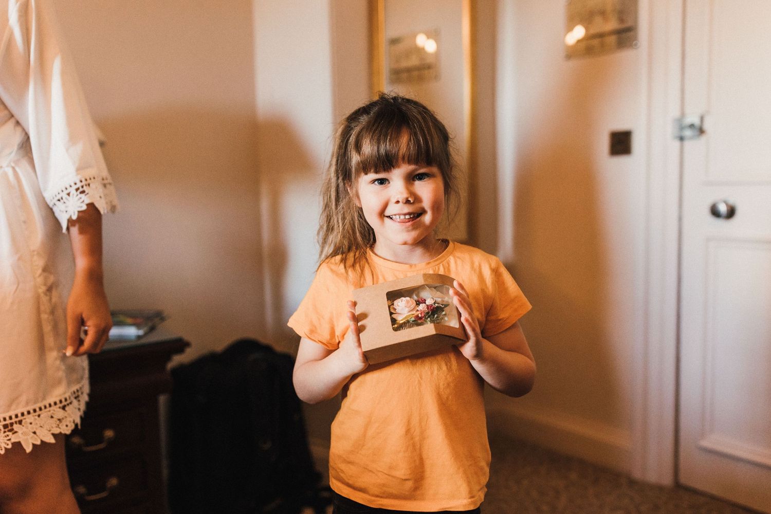 Child in orange t-shirt holding something indoors with joyful expression.