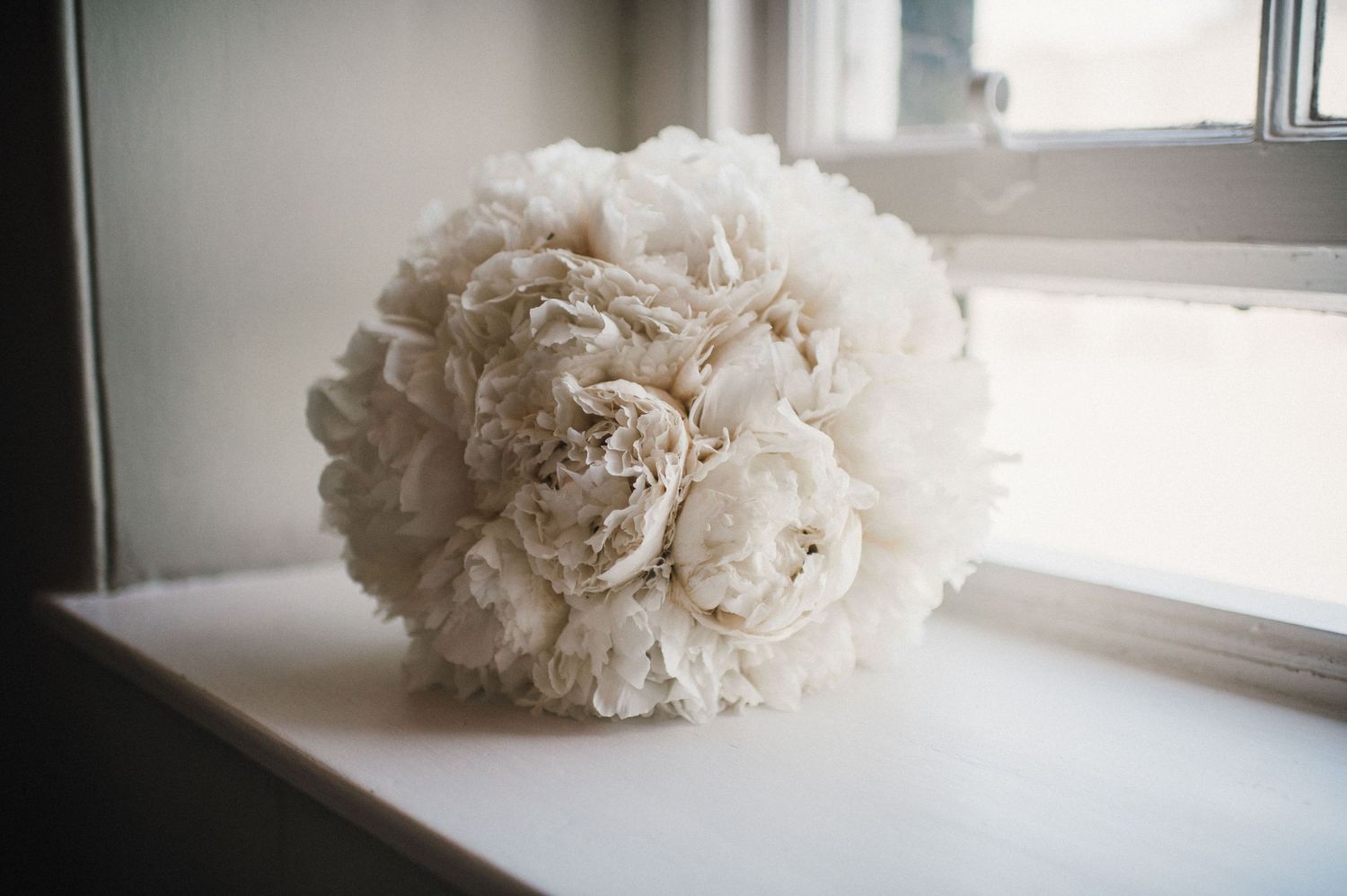 A delicate white peony bouquet rests on a windowsill in natural light.