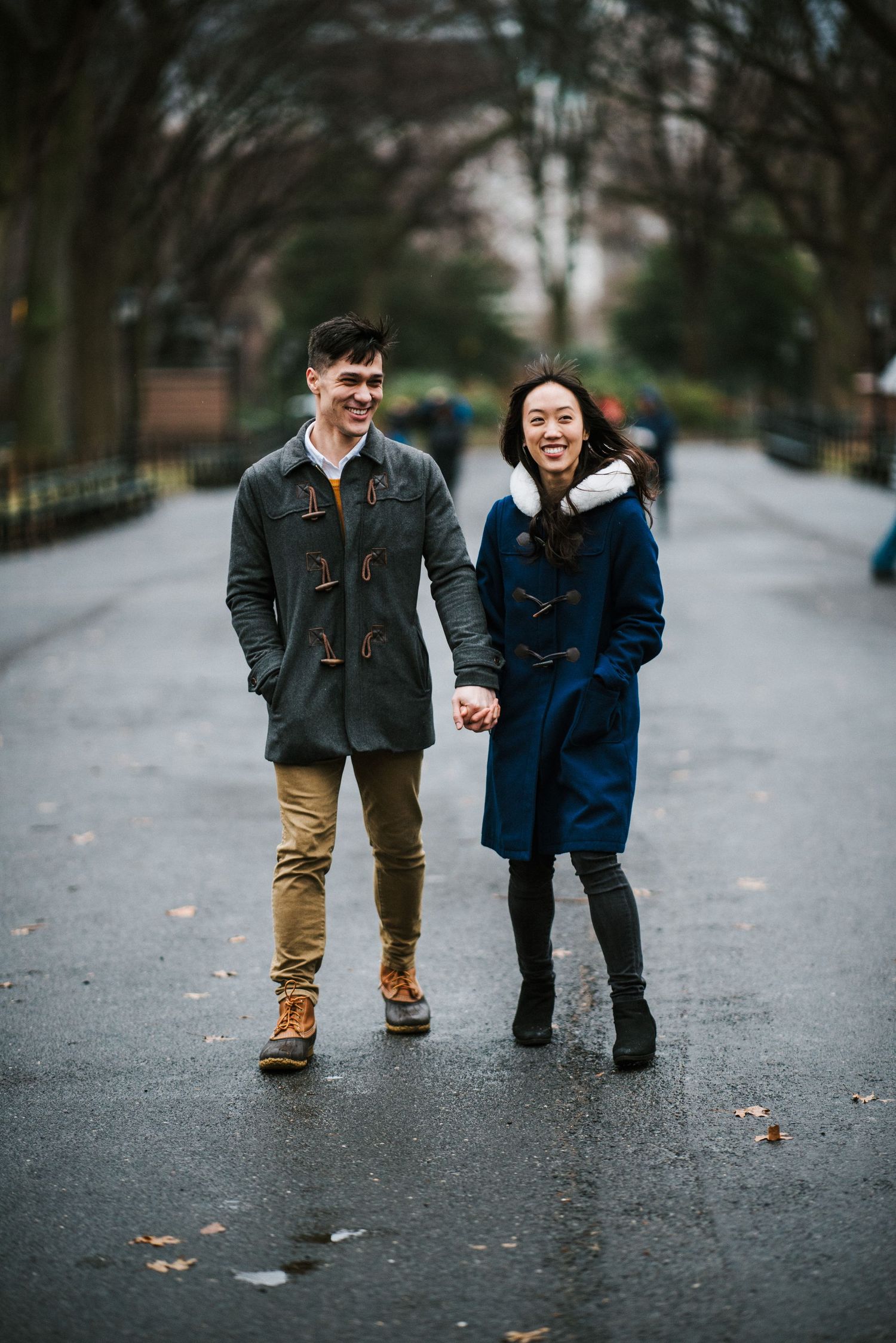 A couple enjoys a winter walk together on a path in Central Park with NYC buildings in the background.