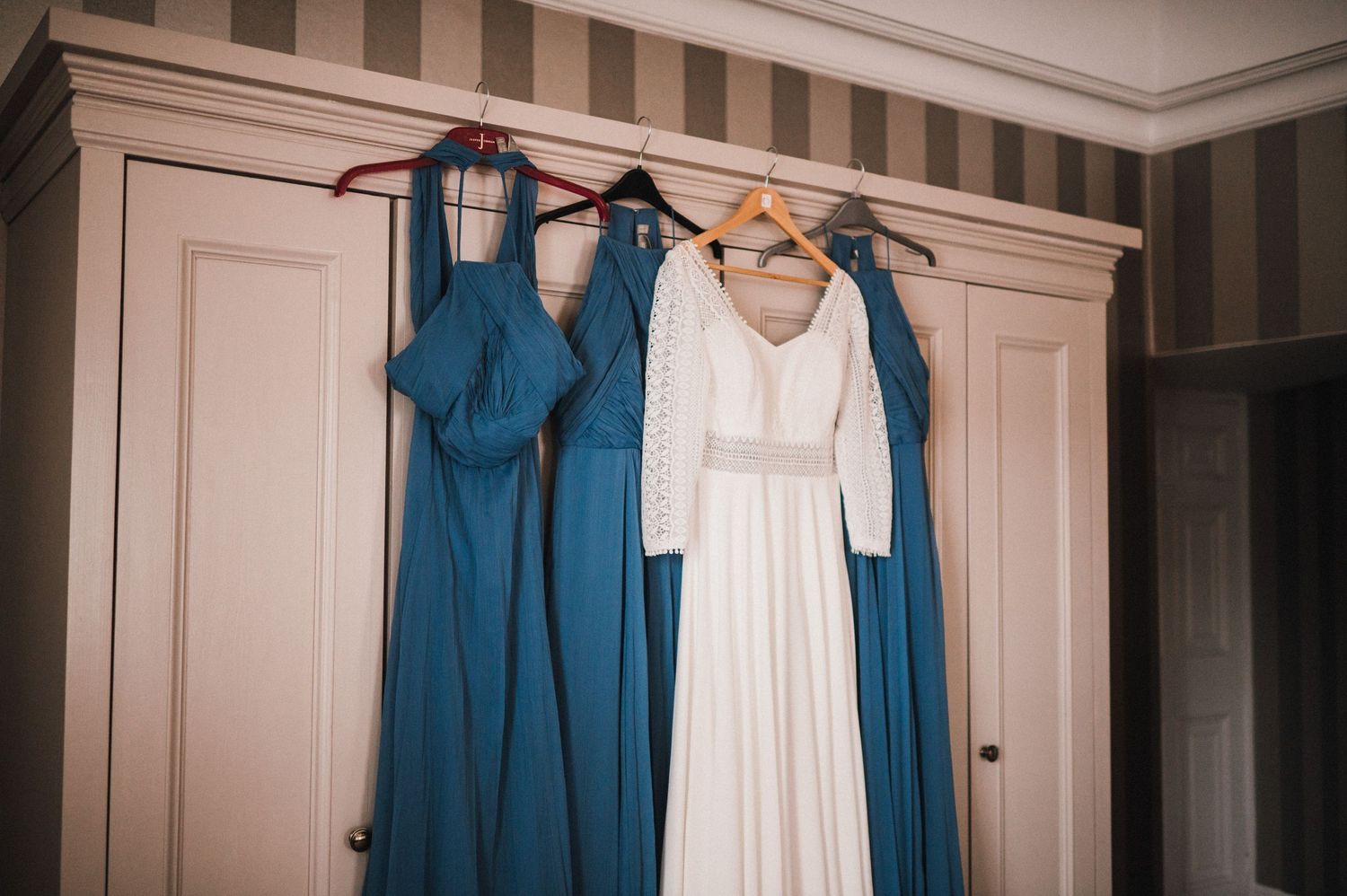 Wedding dresses in white and teal blue hanging on wooden wardrobe.