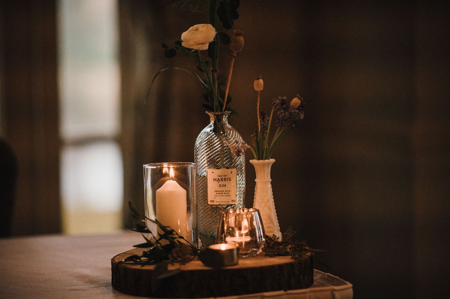 Vintage-style table decor with glass bottles, candles and flowers on wooden serving board.