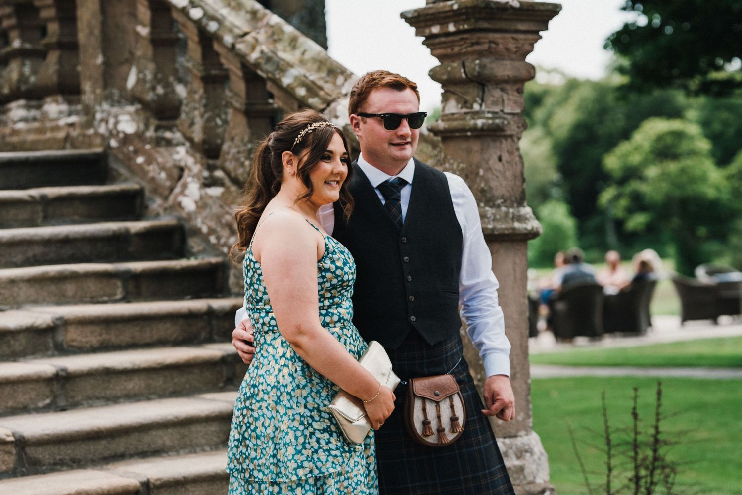 Couple in formal wedding attire pose together near stone architecture outdoors.