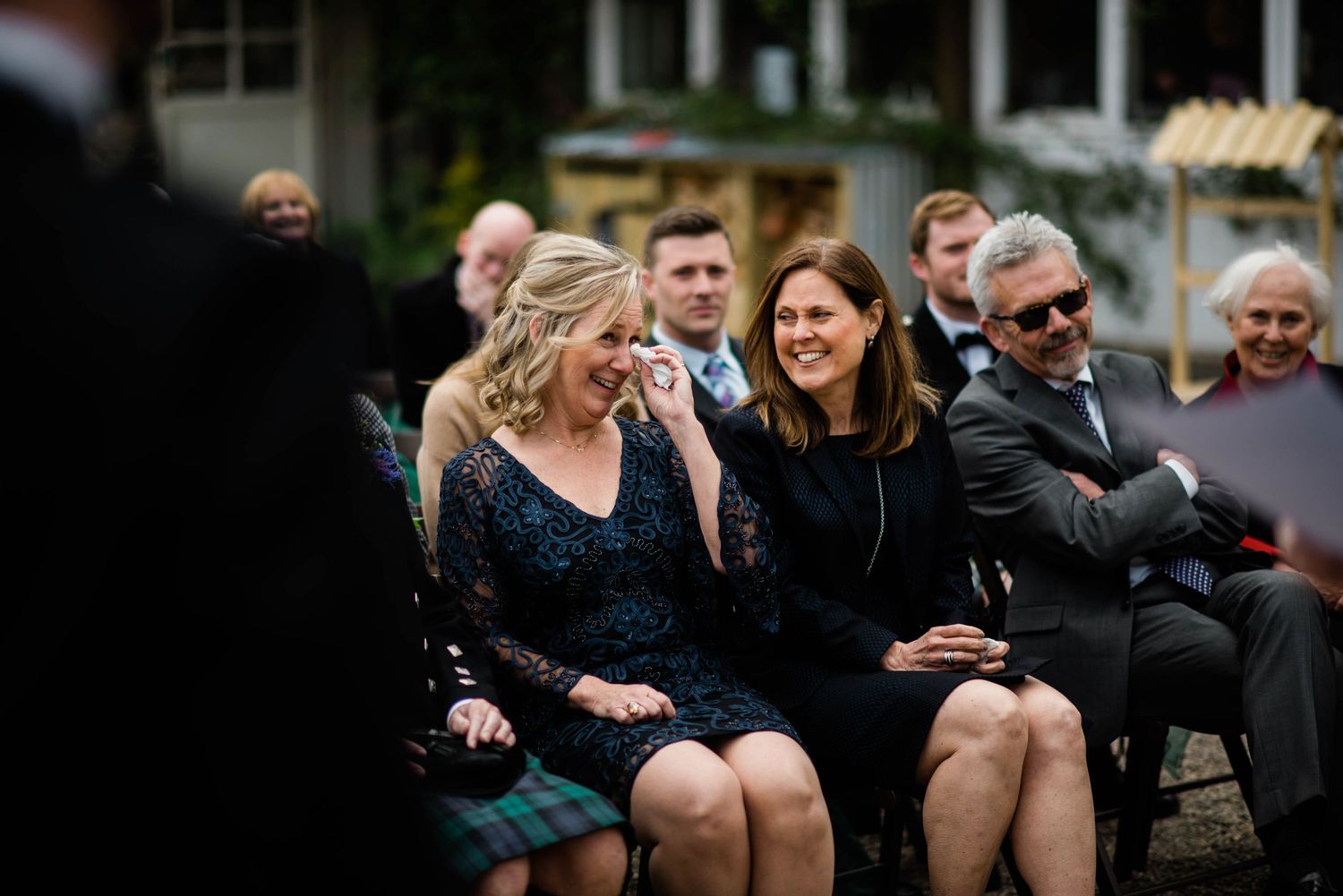 Wedding guests seated outdoors sharing a light moment during the ceremony.