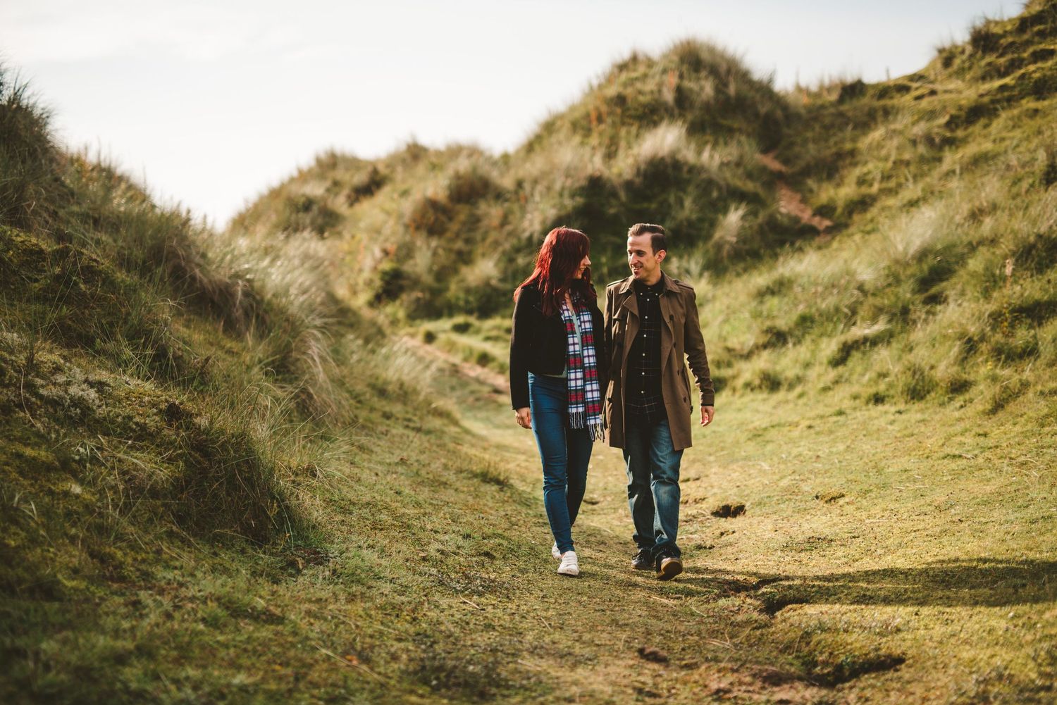 A couple walking together on a winding dirt path through green hillsides.
