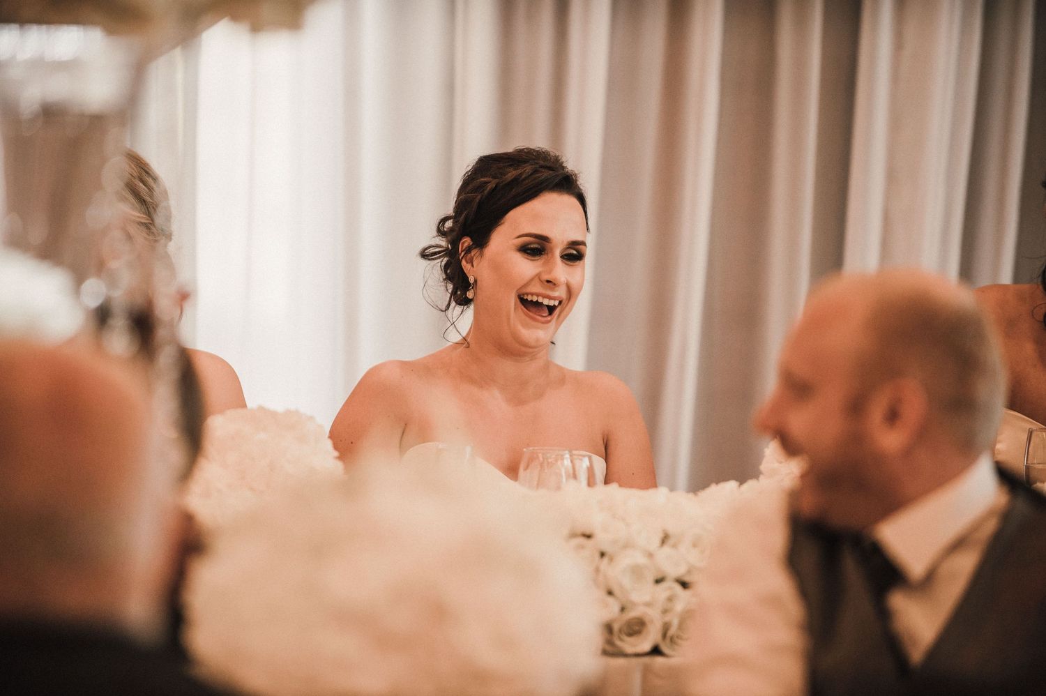 Candid moment of laughter during wedding reception speeches at decorated venue.