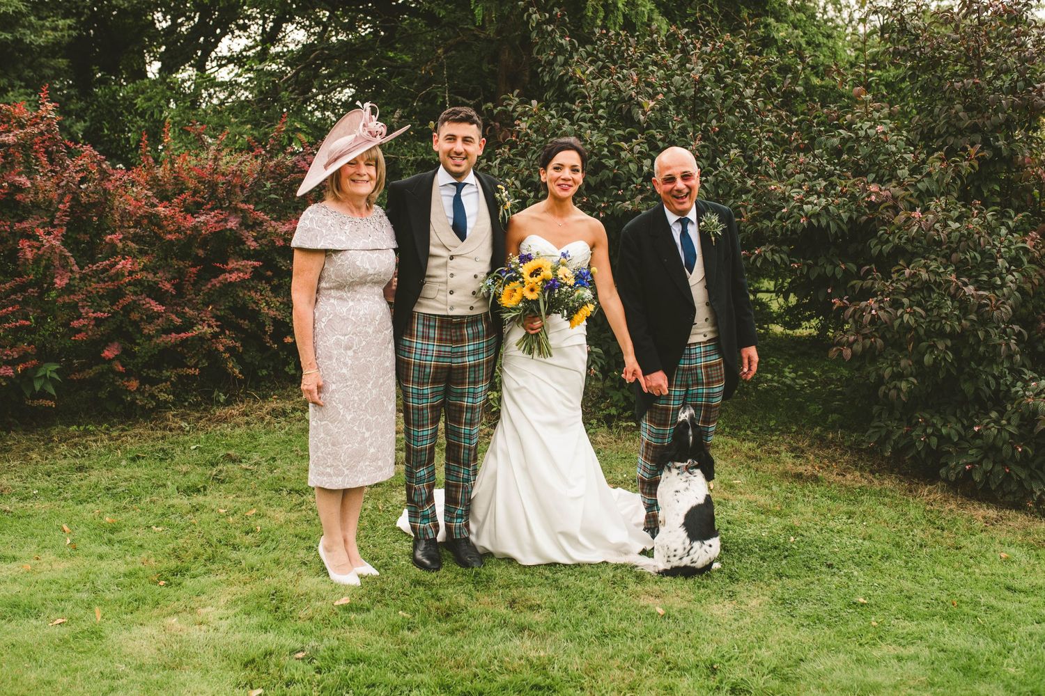 Small wedding group poses on lawn wearing traditional Scottish formal attire.
