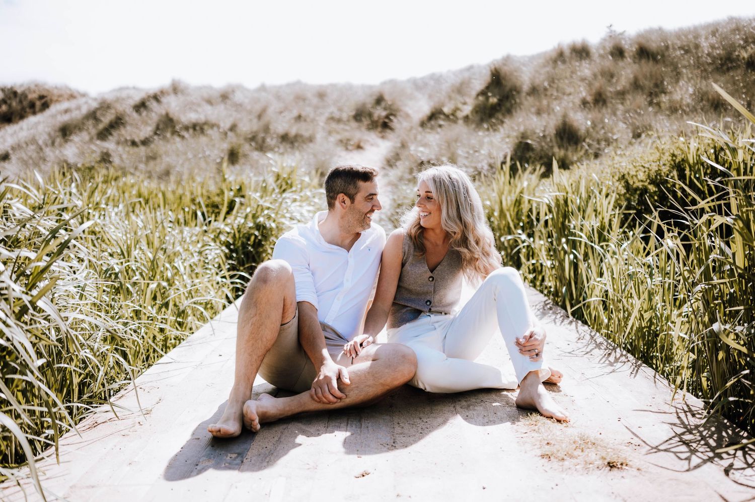Engagement photography session Aberdeen. A couple relaxes together on sandy dunes surrounded by coastal grass.
