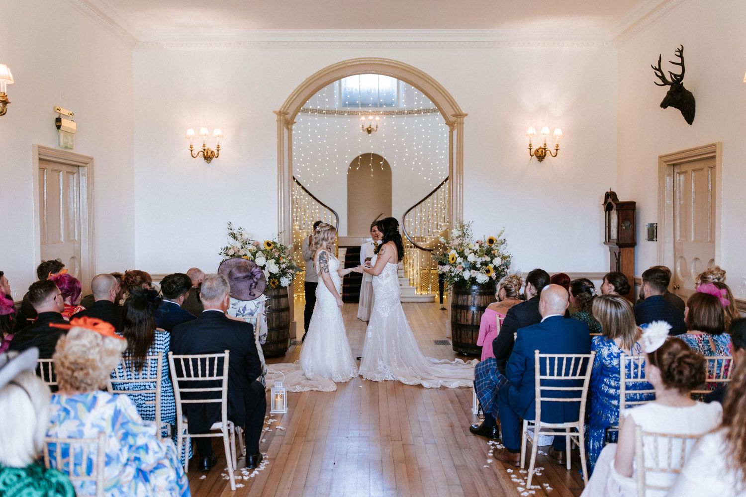 Wedding ceremony in elegant white room with arched doorways and floral decorations.