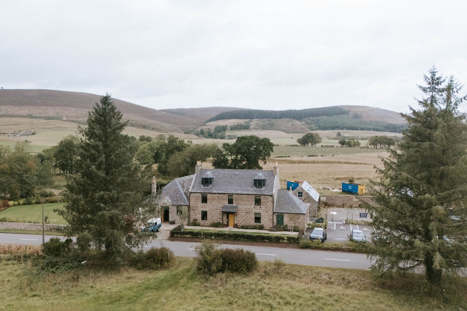 A rustic stone house nestled in the Scottish highlands with rolling hills in the background.
