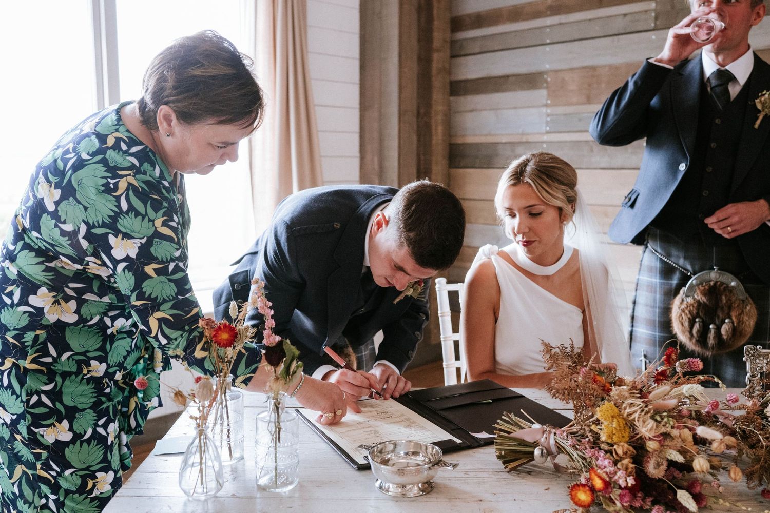 Wedding guests signing the marriage register at a rustic venue with autumn decorations.